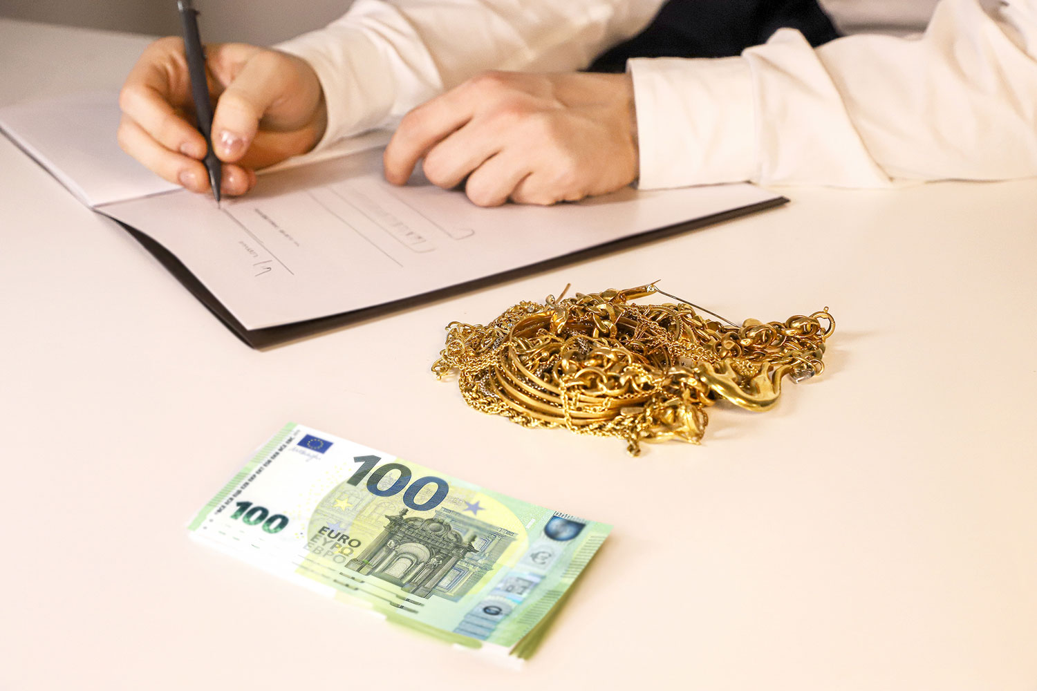una persona firma di contratto di compravendita di gioielli in oro usato, in cambio si vedono alcune banconote da 100 Euro sul tavolo